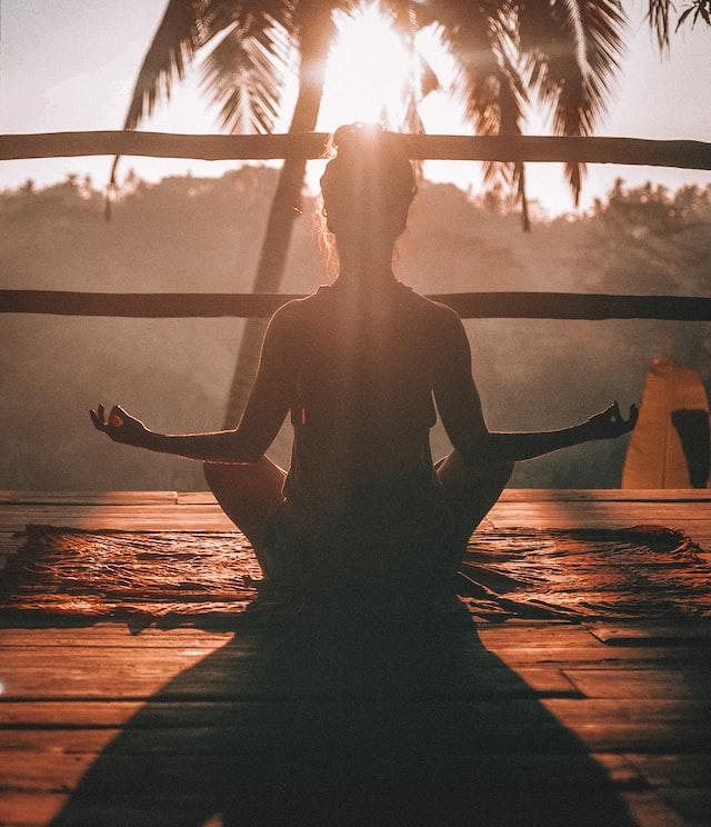 Image of a woman sitting in meditation at sunset. In the photo we can have a sense of calm and balance that represents a lot about Ayurveda.