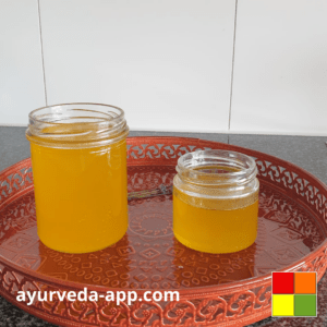 Photo of two glass jars filled with Ghee, still liquid, on top of a decorated red tray.