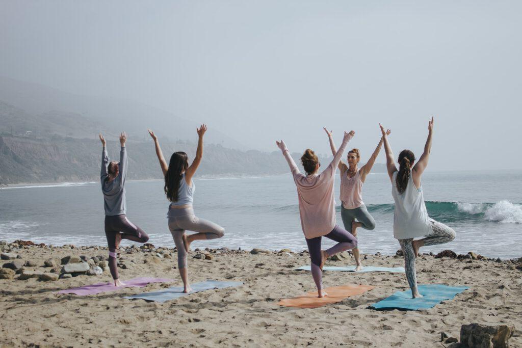 Image of women doing yoga, standing on one foot, on the beach. You need to reach your balance weight to live healthier and happier.