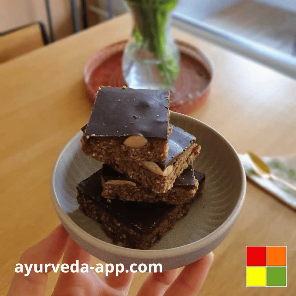 Photo of a bowl full of Nutty chocolate bars. You can see a hand holding the bowl, and in the background there is a vase of flowers.