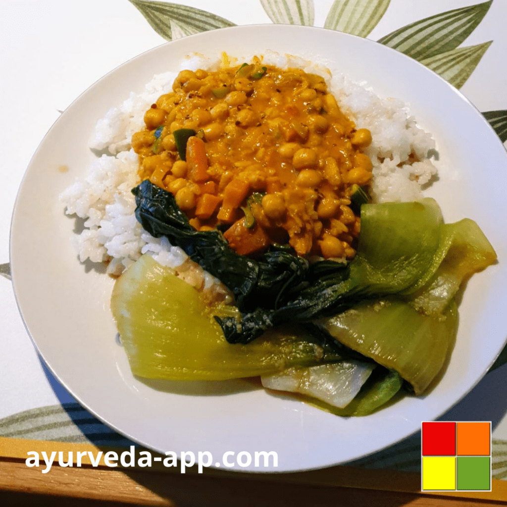 Photo of Chickpea curry with pak choi served on a white plate over rice.