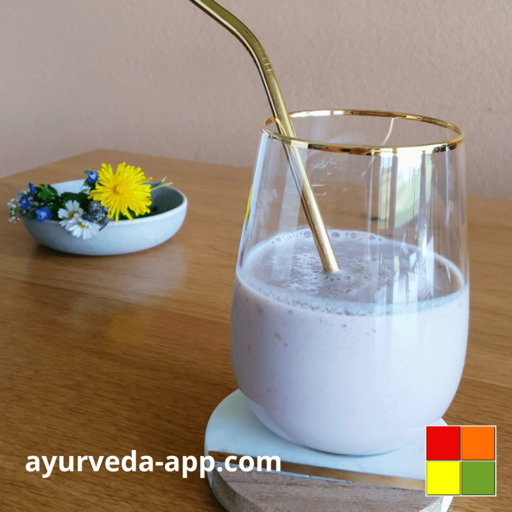 Photo of Raspberry Banana Smoothie served in a gold-rimmed glass tumbler with a gold-tone metal straw. Next to it is a bowl of colorful flowers to decorate.
