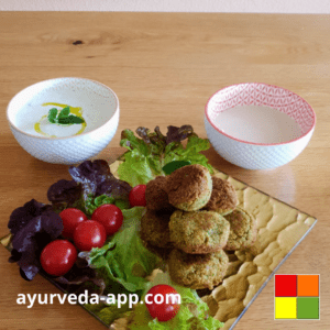 The image shows a golden dish with falafel accompanied by a salad of lettuce and cherry tomatoes. Next to the plate are two bowls of sauces.