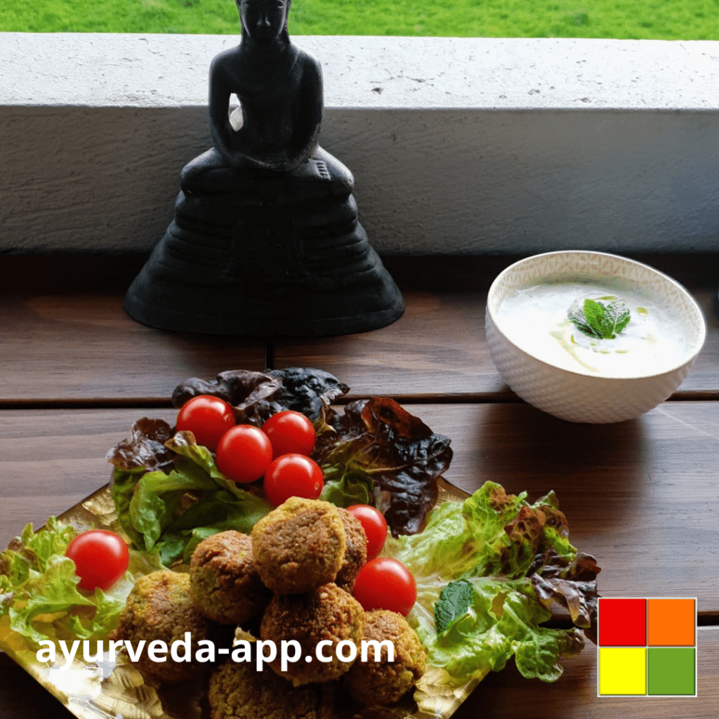 The image shows a golden dish with falafel accompanied by a salad of lettuce and cherry tomatoes. Beside the plate is a bowl of sauce.