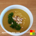 Photo of Cashew pumpkin leek soup served in a white bowl, topped with cashews and fresh herbs for garnish.