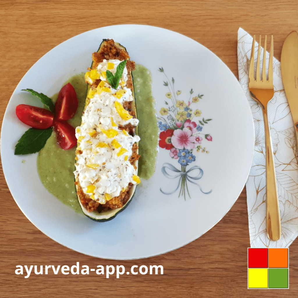 Pictured is a Stuffed Zucchini boat on top of broccoli sauce on a flowery white plate, along with a cherry tomato and herbs for garnish.