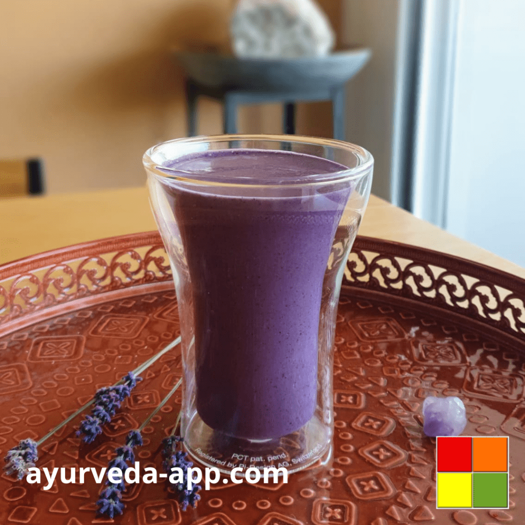 Photo of a glass with the detox energy smoothie. The glass is on a tray, decorated with a purple crystal and lavender flower