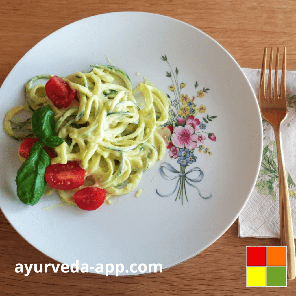 Photo of a flowery plate with Zoodles with vegan cheese sauce. Next to the plate is a napkin with a golden fork.