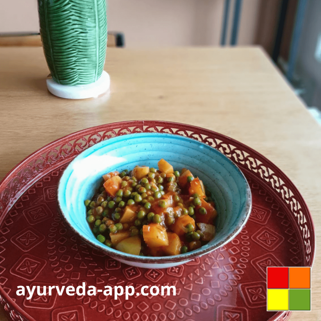 Photo of potatoes-peas stew recipe in a blue bowl on top of a decorated red tray. In the background of the image, you can see a decorative green vase.