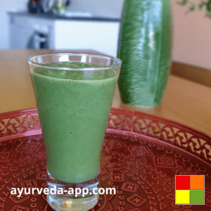 Photo of a glass of celery-avocado detox smoothie on a well-decorated red tray. In the background there is a green vase