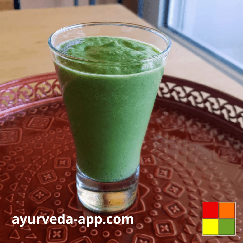 Photo of a glass of celery-avocado detox smoothie on a well-decorated red tray. In the background there is a green vase