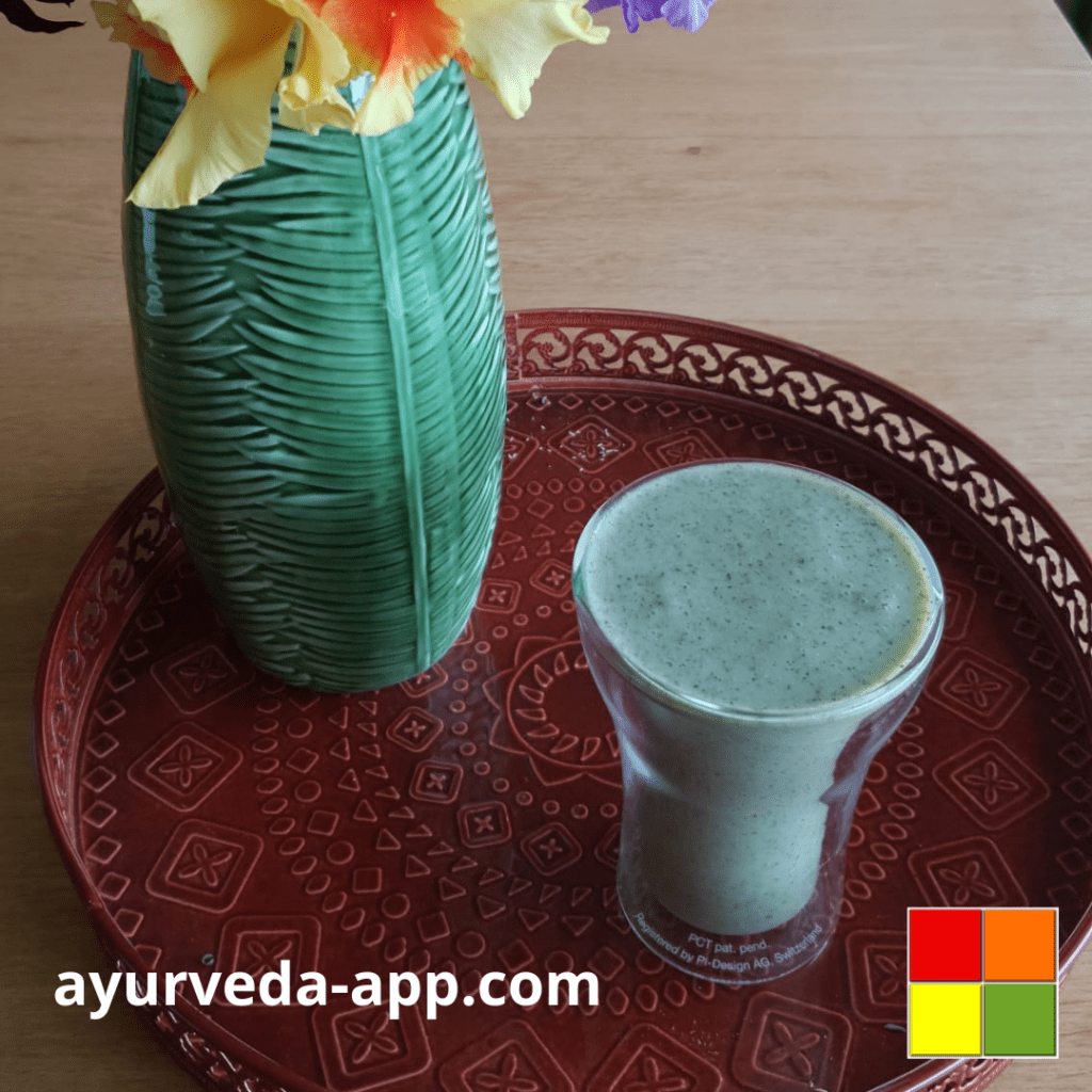 Photo of a double glass glass of glowy skin smoothie on top of a decorated red tray, along with a green flower vase.