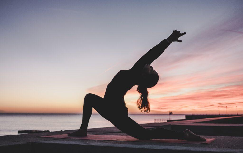 Photo of a woman doing Yoga facing the sea at sunset. Yoga and Ayurveda are interconnected philosophies