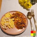 Photo of a flat plate with Bean Stew with pasta. Next to the plate is a golden fork and knife and decorative flowers.