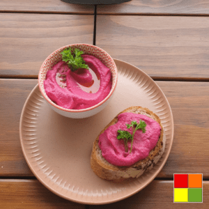 Photo of a wide flat plate with a bowl of Pinky Hummus, and a piece of toast with the hummus on the side