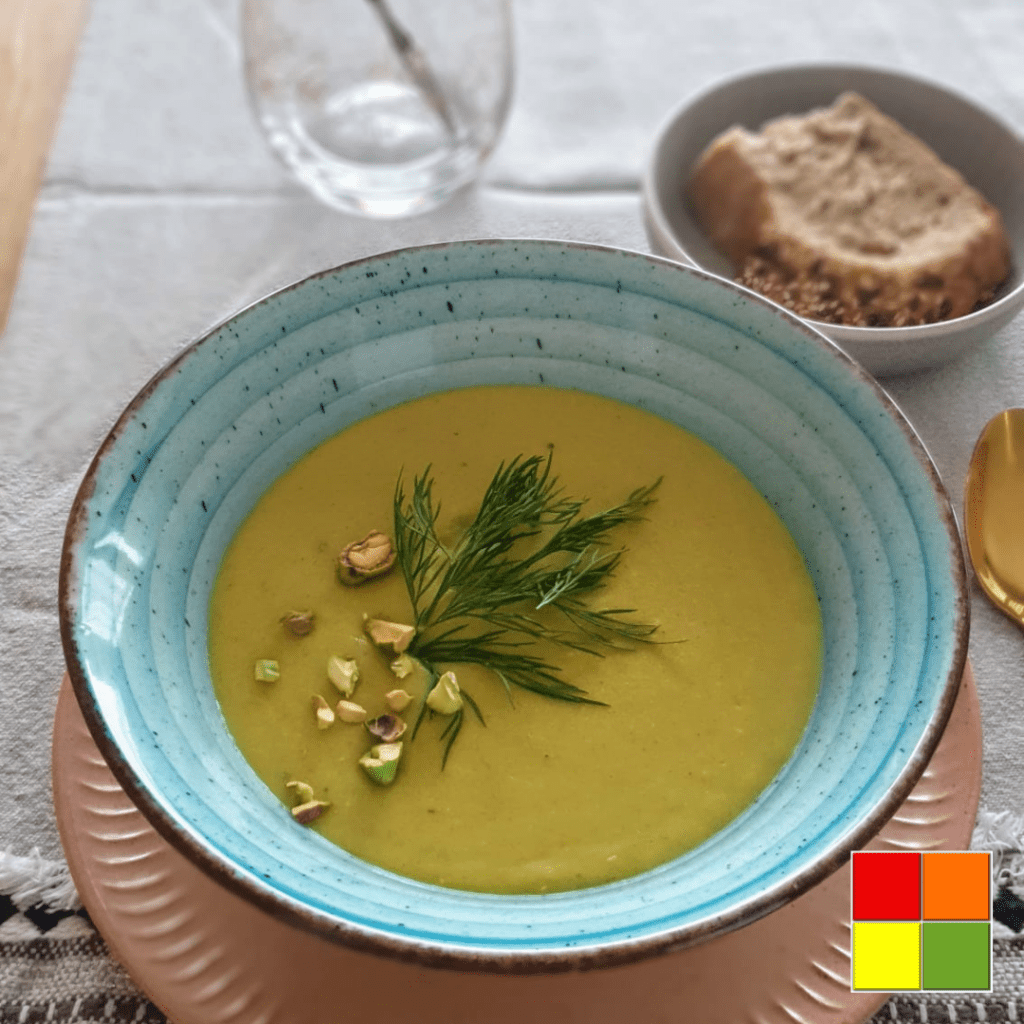 Photo of Cauliflower pumpkin soup in a blue bowl with a brown rim. Next to the bowl is a golden spoon.