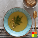 Photo of Cauliflower pumpkin soup in a blue bowl with a brown rim. Next to the bowl is a golden spoon.