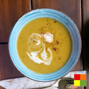 Sopa cremosa de ervilha servida em uma tigela de cerâmica azul, coberta com um fio de creme de leite e uma pitada de especiarias.