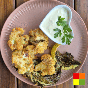 Picture of Baked cauliflower with vegan horseradish dip served on a light pink round plate. The dip sauce is in a small heart-shaped ceramic bowl.