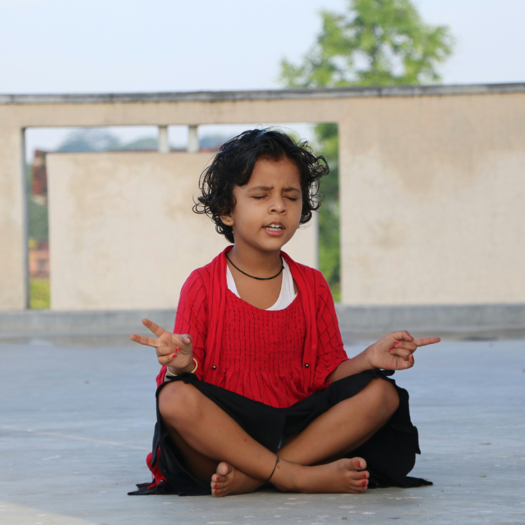 Yoga for Kids meditation pose with a young child sitting cross-legged, eyes closed, practicing mindfulness and breathing exercises outdoors.
