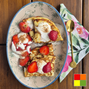 Soft and fluffy Low Carb Pancakes topped with fresh strawberries, cream, and cinnamon, served on a decorative plate.