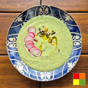 Cooling Cucumber Avocado Soup with Kefir topped with sliced radishes, pumpkin seeds, mixed nuts, and a drizzle of olive oil, served in a blue patterned bowl.